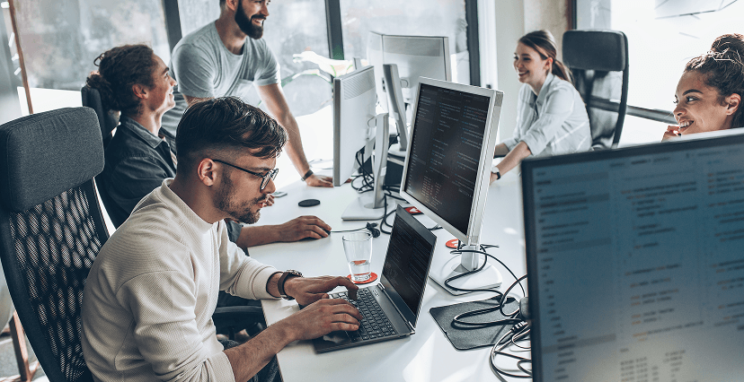 tres personas trabajando juntas con portátiles y monitores en una oficina