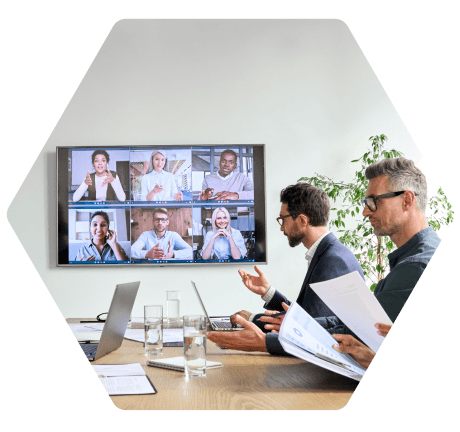equipo de profesionales en una sala de juntas manteniendo una videoconferencia con varios participantes en una pantalla grande